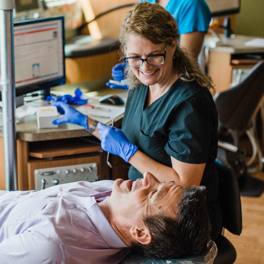 Dr. Lyons is laughing with a man wearing a purple dress shirt in her treatment chair.