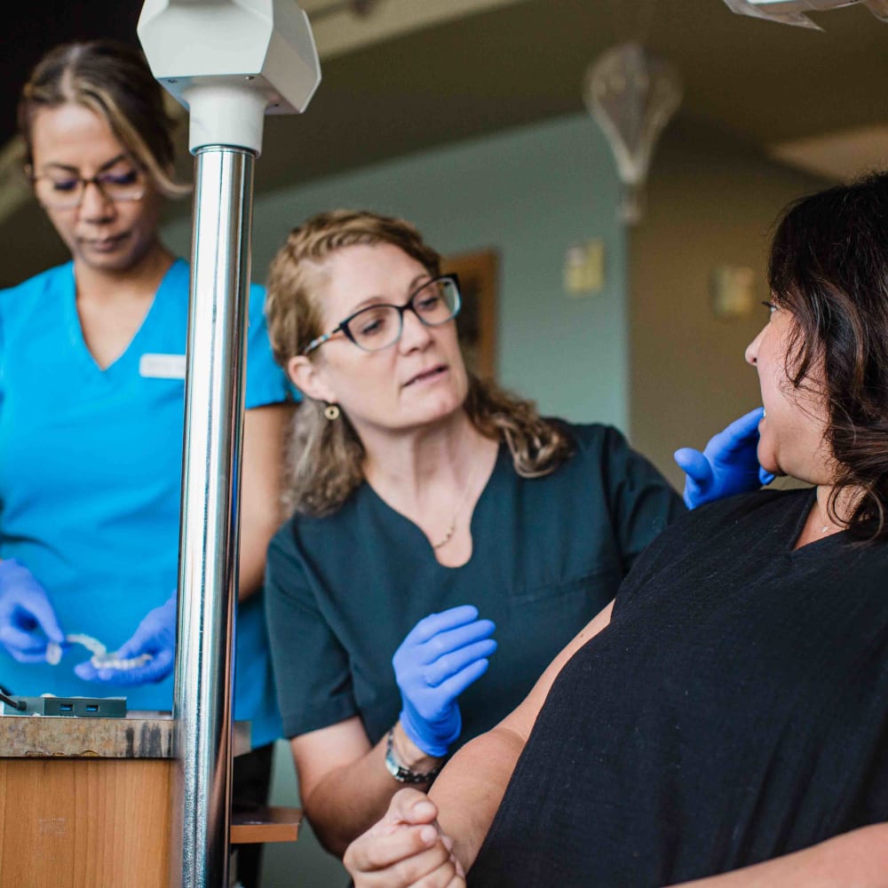 Dr. Lyons checking a patient's teeth while a team member standing behind her prepares Invisalign clear aligners.