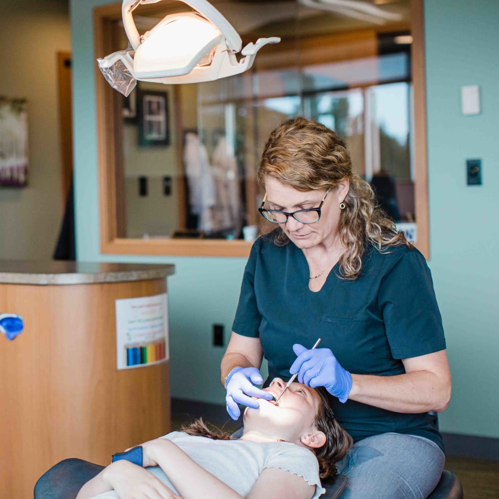 Dr. Lyons is inspecting the teeth of a young girl in her treatment chair.