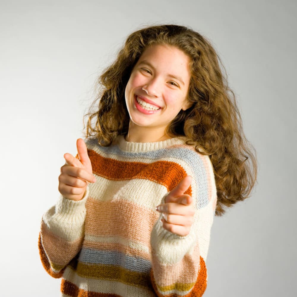 A young woman is smiling while holding up both hands pointing at the camera.