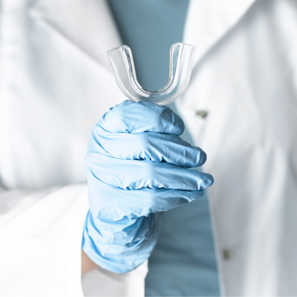 Clinic staff person, wearing white coat and blue gloves, holding up a sports guard.