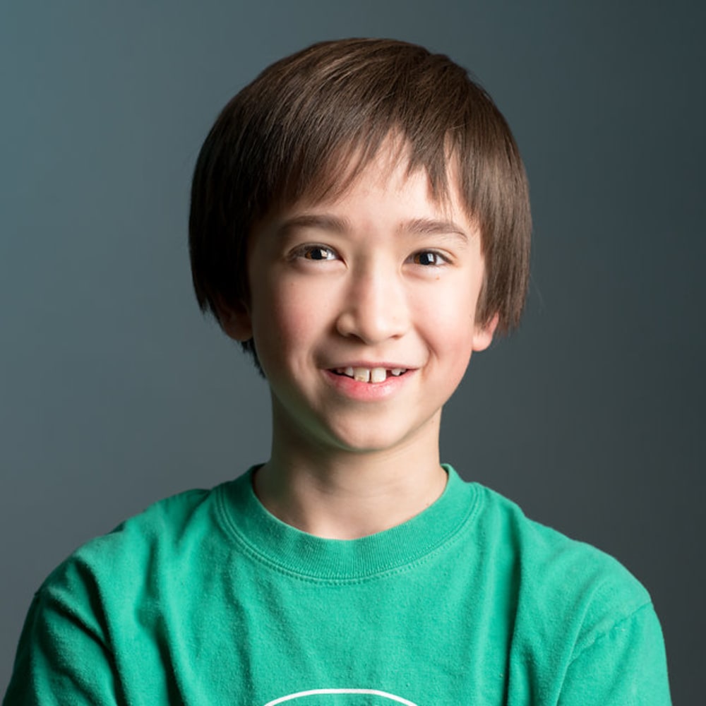 A kid in a green t-shirt with gaps in his front teeth is smiling.