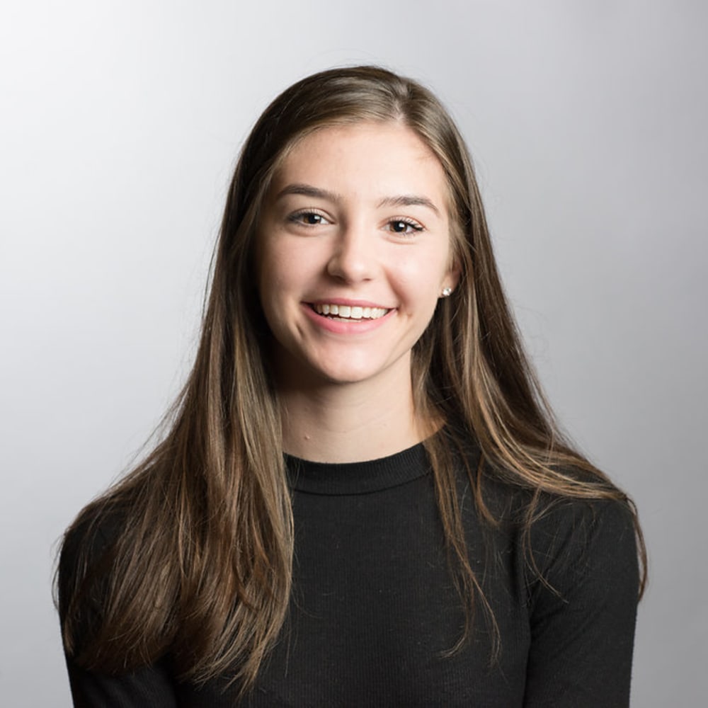 A teenage girl in a black shirt with long brown hair smiles.